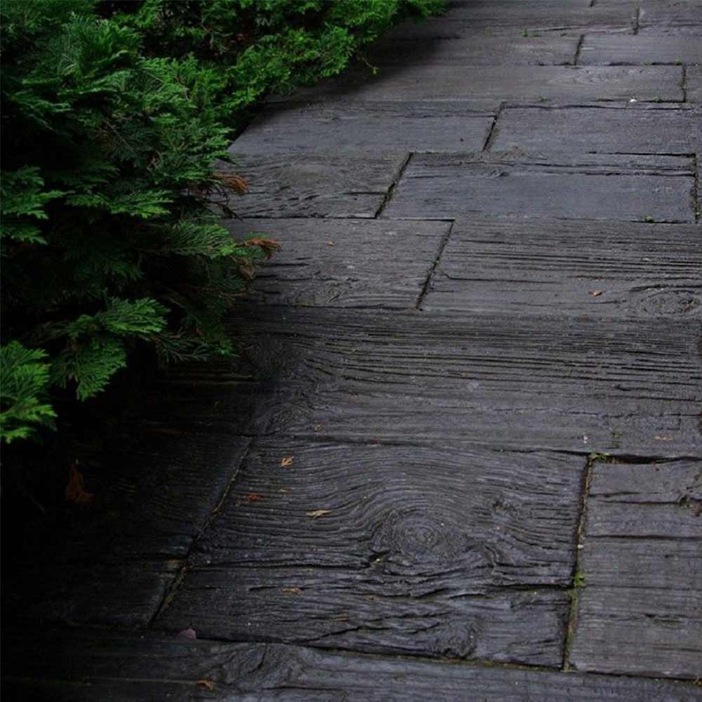 Ein dunkler, nasser Holzweg aus alten Holzplanken neben üppigen grünen Thujen im Garten