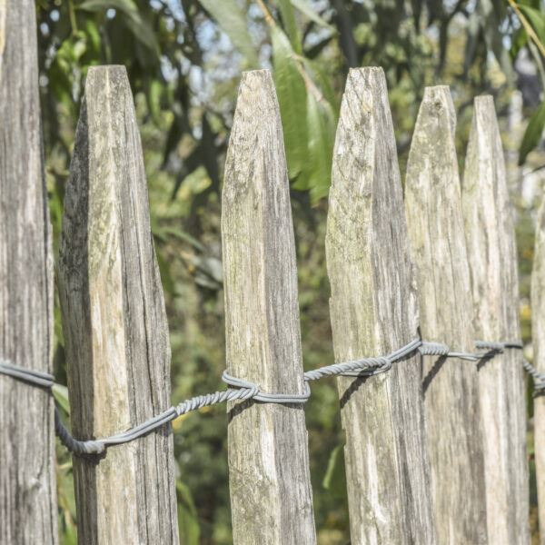 Nahaufnahme eines alten Holzzauns aus zugespitzten Latten, die mit gedrehtem Metalldraht verbunden sind