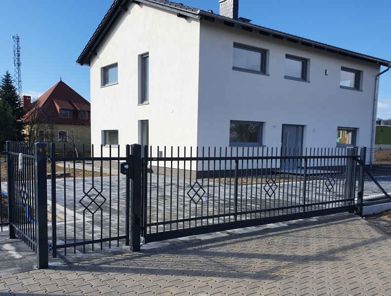 Weißes Einfamilienhaus mit modernem schwarzem Metallzaun und gepflasterter Einfahrt im Vordergrund