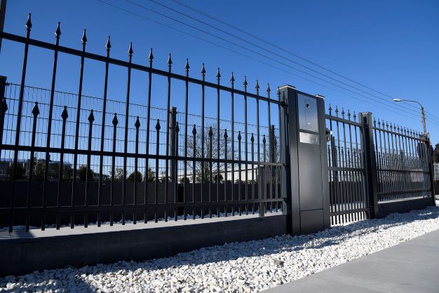 Schwarzer Metallzaun mit dekorativen Spitzen und grauen Betonsäulen, umgeben von Schnee an einem sonnigen Wintertag