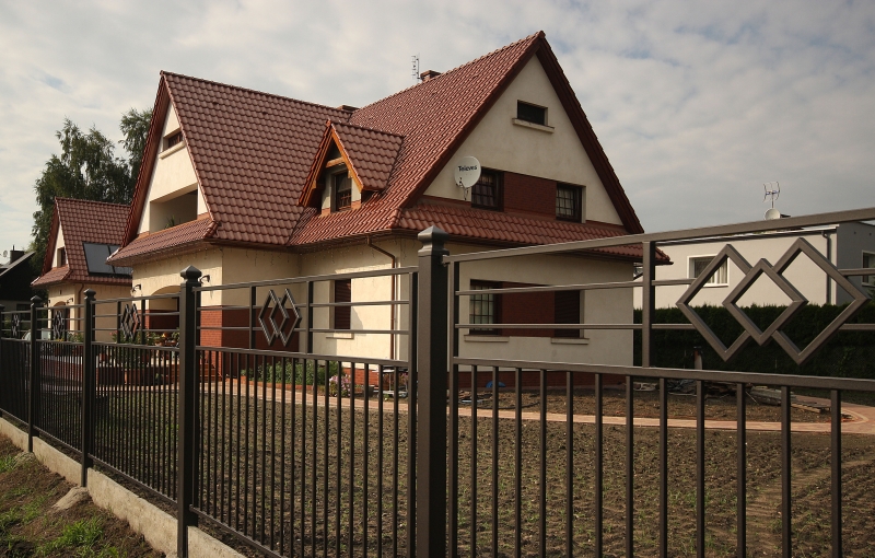 Elegantes Einfamilienhaus mit braunem Ziegeldach, beiger Fassade und dekorativem Metallzaun im Vorgarten