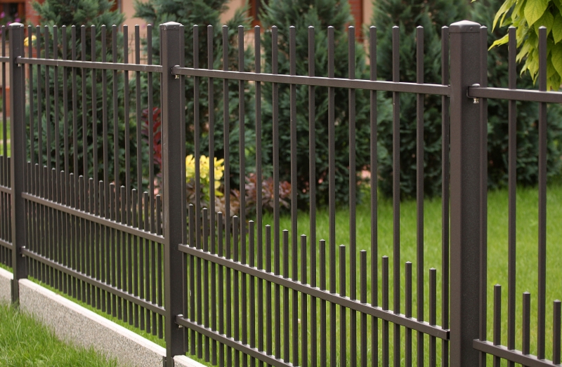 Eleganter anthrazitfarbener Metallzaun mit vertikalen Stäben unterschiedlicher Höhe im gepflegten Garten