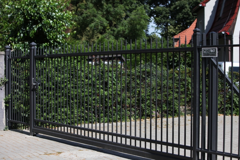 Ein elegantes schwarzes Schiebetor aus Metall vor einem Garten, mit vertikalen Stäben und moderner Konstruktion