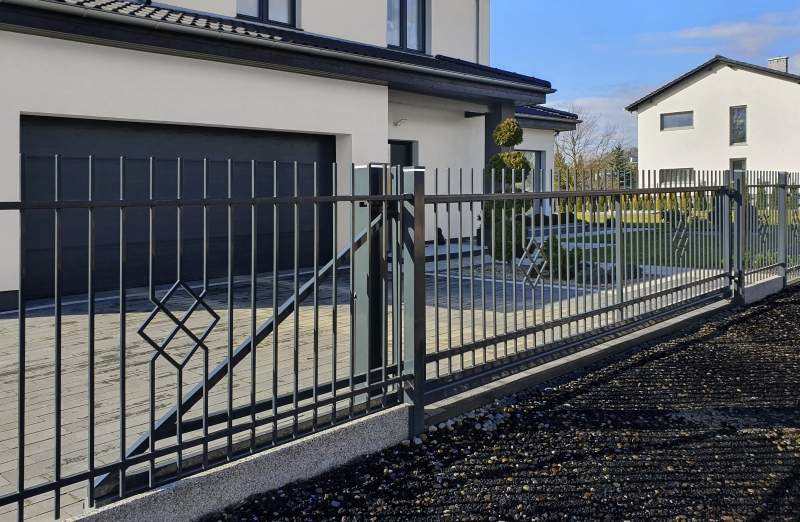 Eleganter anthrazitfarbener Metallzaun mit geometrischem Muster vor einem modernen weißen Haus mit Garage