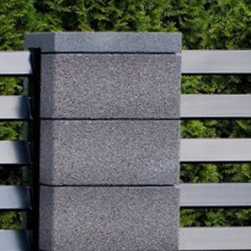 Grauer Betonpfosten mit horizontalen Metalllamellen als Teil eines modernen Gartenzauns vor grünem Hintergrund