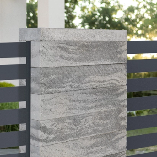 Grauer Betonpfeiler mit wellenförmiger Textur, montiert an einem modernen Metallzaun im Außenbereich
